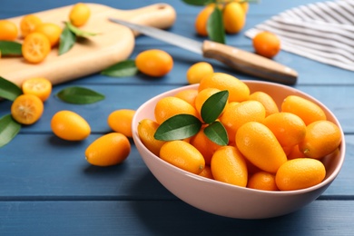 Fresh ripe kumquats in bowl on blue wooden table, space for text