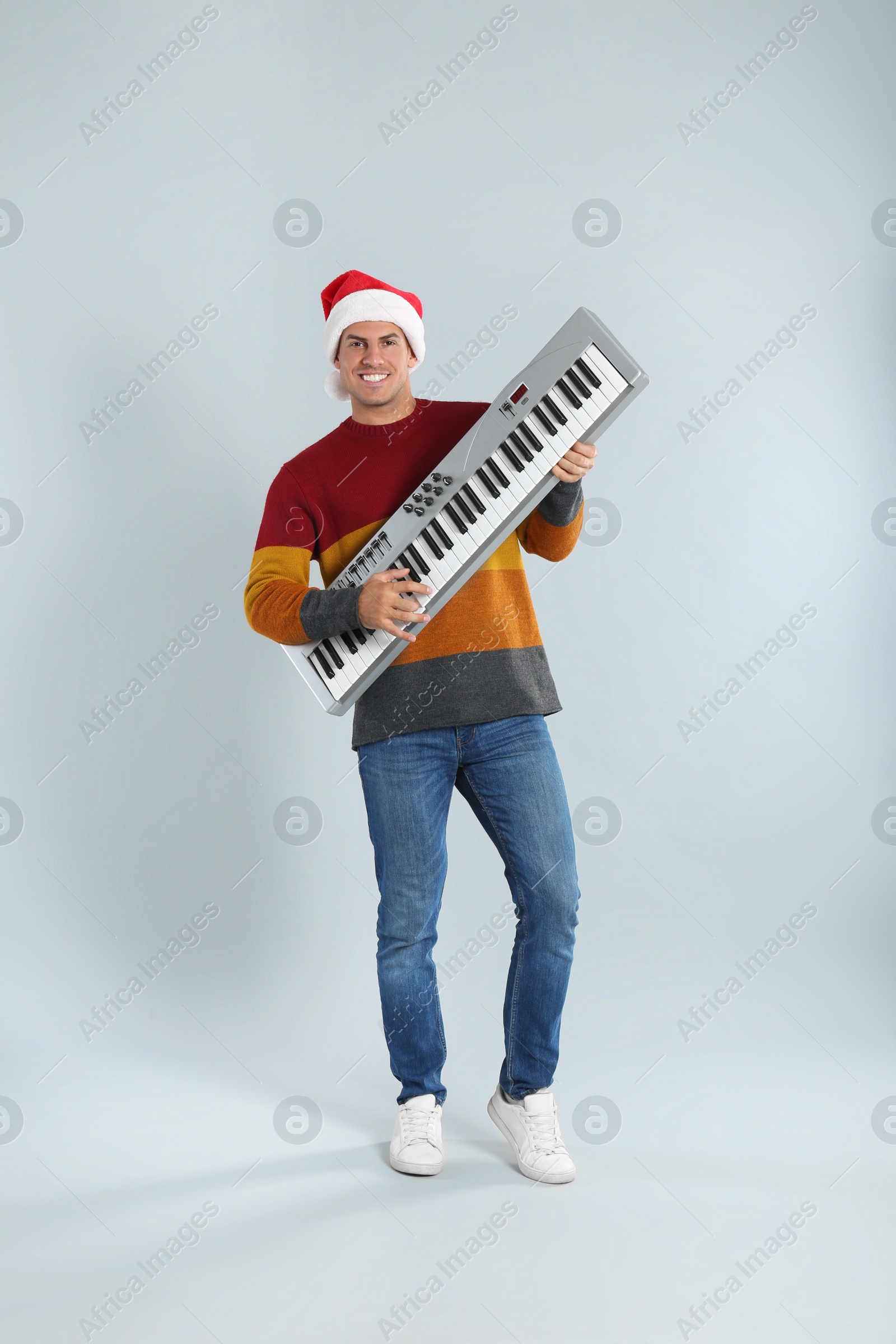 Photo of Man in Santa hat playing synthesizer on light grey background. Christmas music