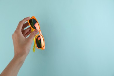 Photo of Woman holding stylish sunglasses on light blue background, closeup. Space for text