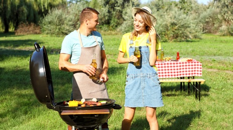 Photo of Happy couple cooking food on barbecue grill in park