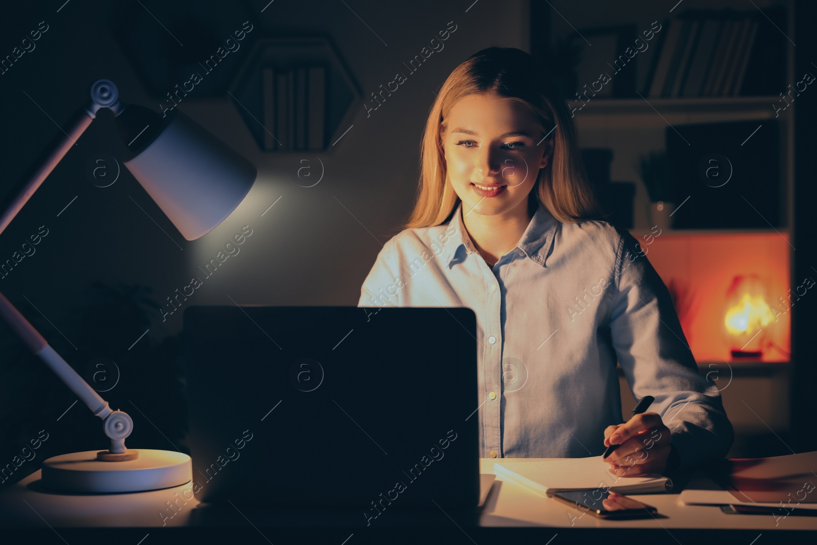 Photo of Home workplace. Woman with pen and notebook working on laptop at white desk in room