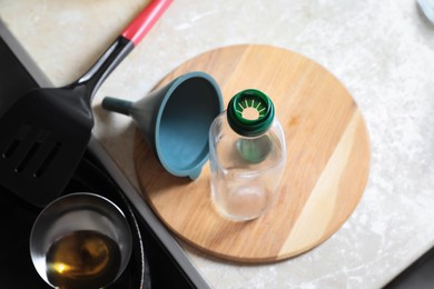 Photo of Empty bottle and funnel near frying pan with used cooking oil in kitchen
