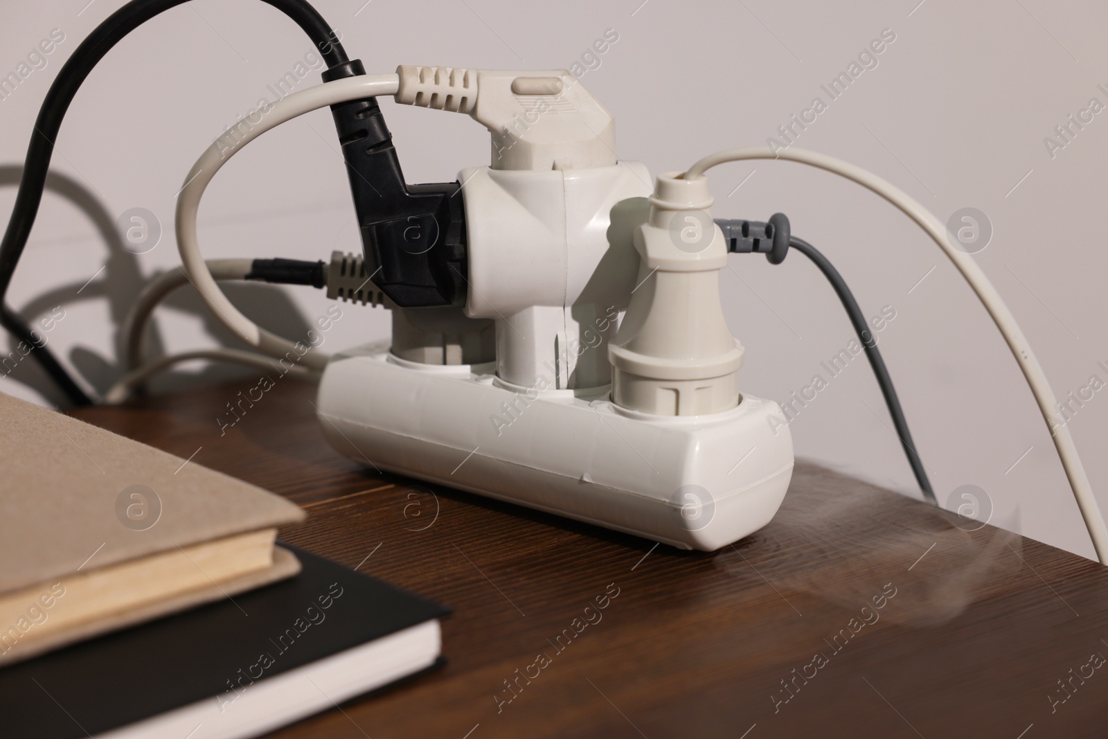 Photo of Smoking plug in power strip on wooden table, closeup. Electrical short circuit