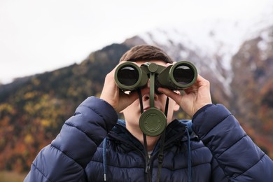 Photo of Boy looking through binoculars in beautiful mountains, closeup