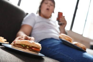 Overweight boy with fast food on sofa at home