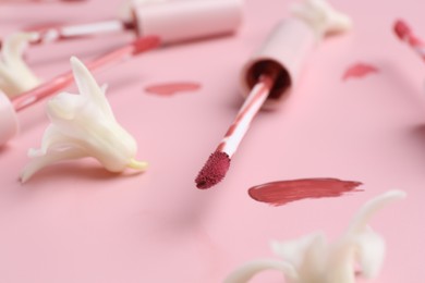 Photo of Color lip glosses, applicators and flowers on pink background, closeup