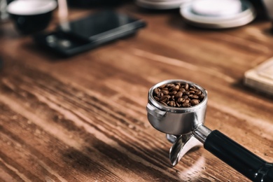 Photo of Portafilter with roasted coffee beans on wooden table. Space for text