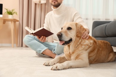 Photo of Man reading book on floor near his cute Labrador Retriever at home, closeup. Space for text