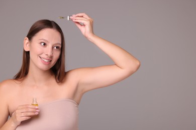 Photo of Beautiful woman applying serum onto hair on grey background, space for text