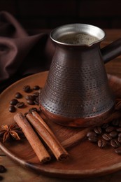 Cezve with Turkish coffee, beans and spices on wooden table, closeup