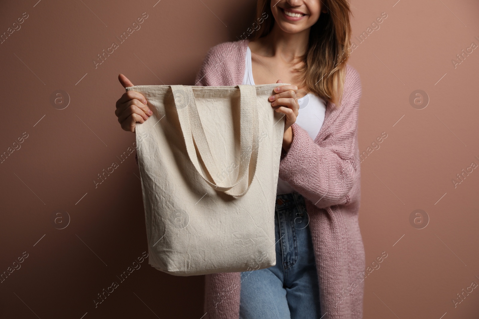 Photo of Happy young woman with blank eco friendly bag against light brown background, closeup