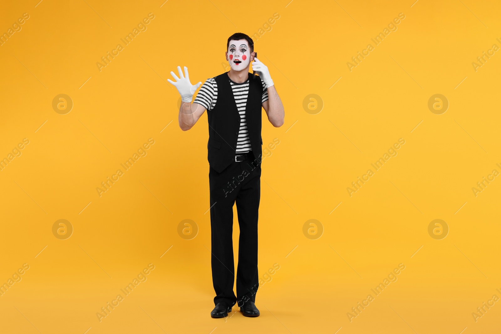 Photo of Funny mime artist talking on phone against orange background