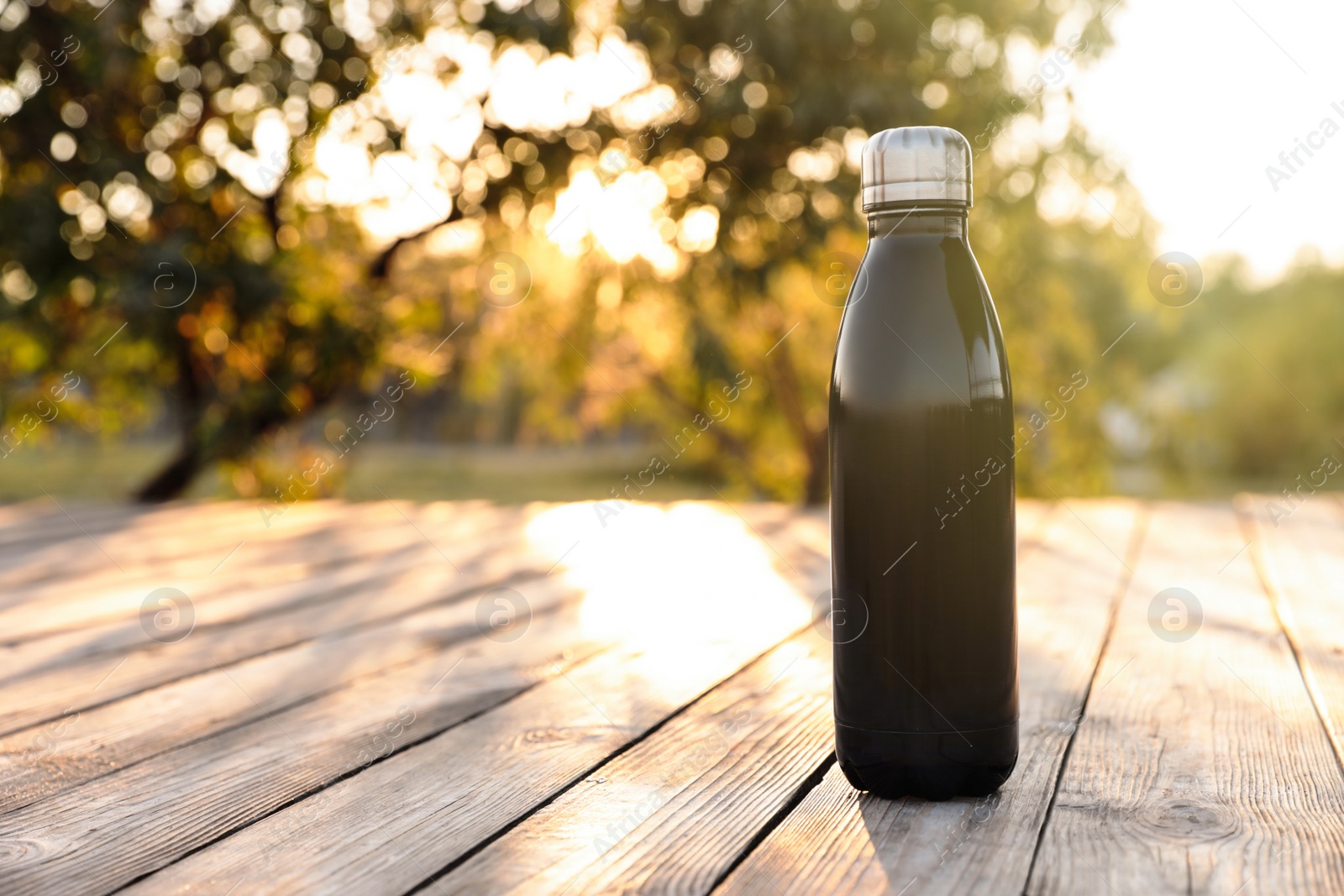 Photo of Modern black thermos bottle on wooden surface outdoors. Space for text
