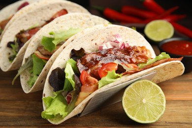 Photo of Delicious tacos with fried bacon and lime on wooden table, closeup