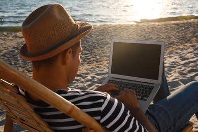 Photo of Man working with laptop in deck chair on beach