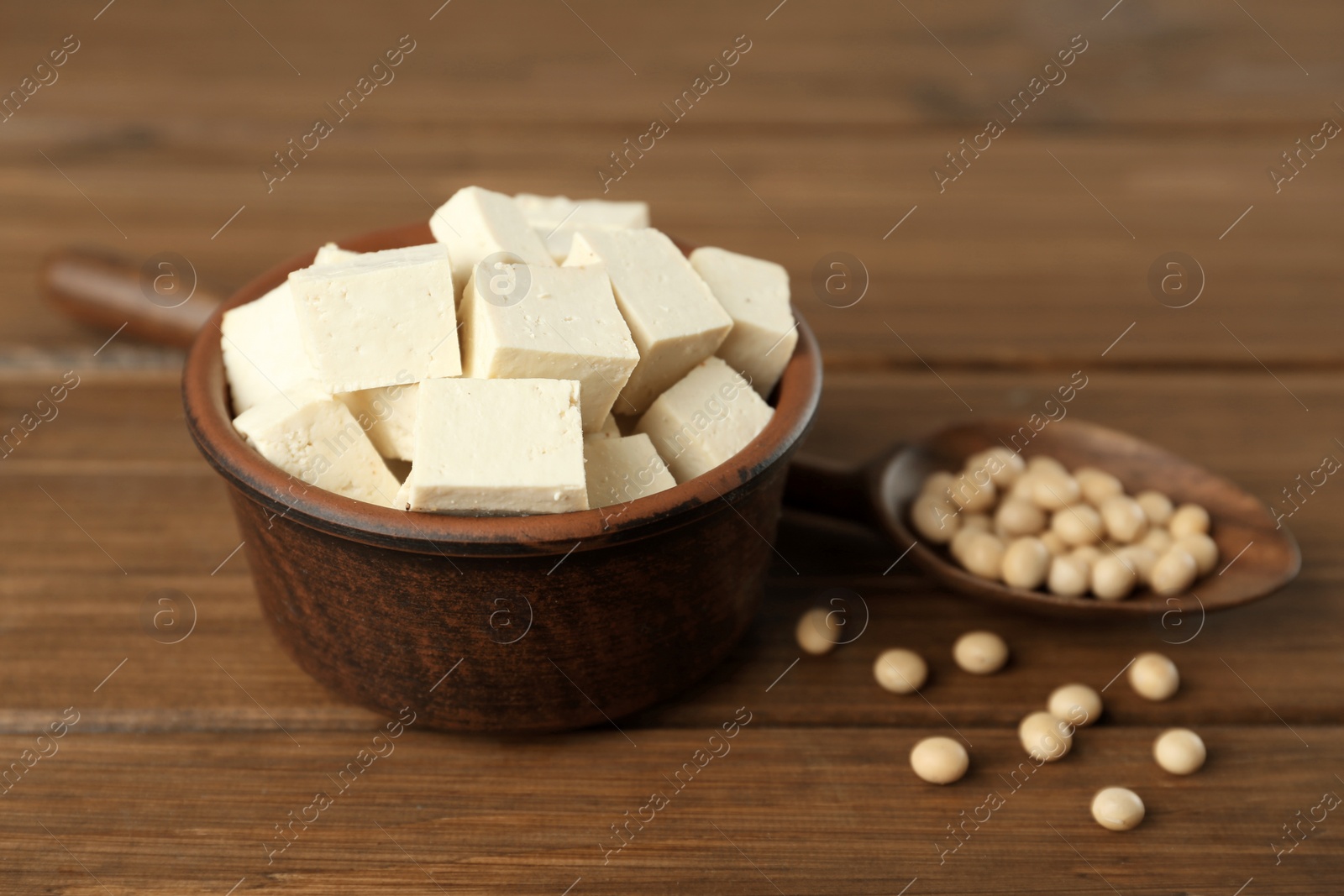 Photo of Pieces of delicious tofu in bowl and soy on wooden table