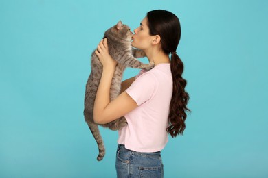 Photo of Young woman kissing her adorable cat on light blue background