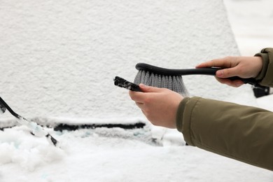 Photo of Woman cleaning car wiper blade from snow with brush, closeup