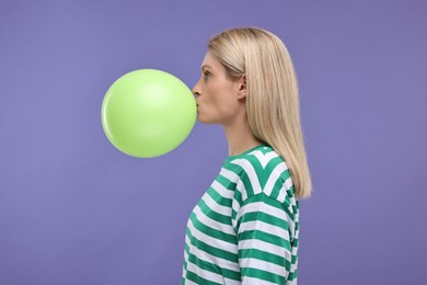 Photo of Woman blowing up balloon on violet background