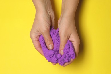 Photo of Woman playing with kinetic sand on yellow background, top view