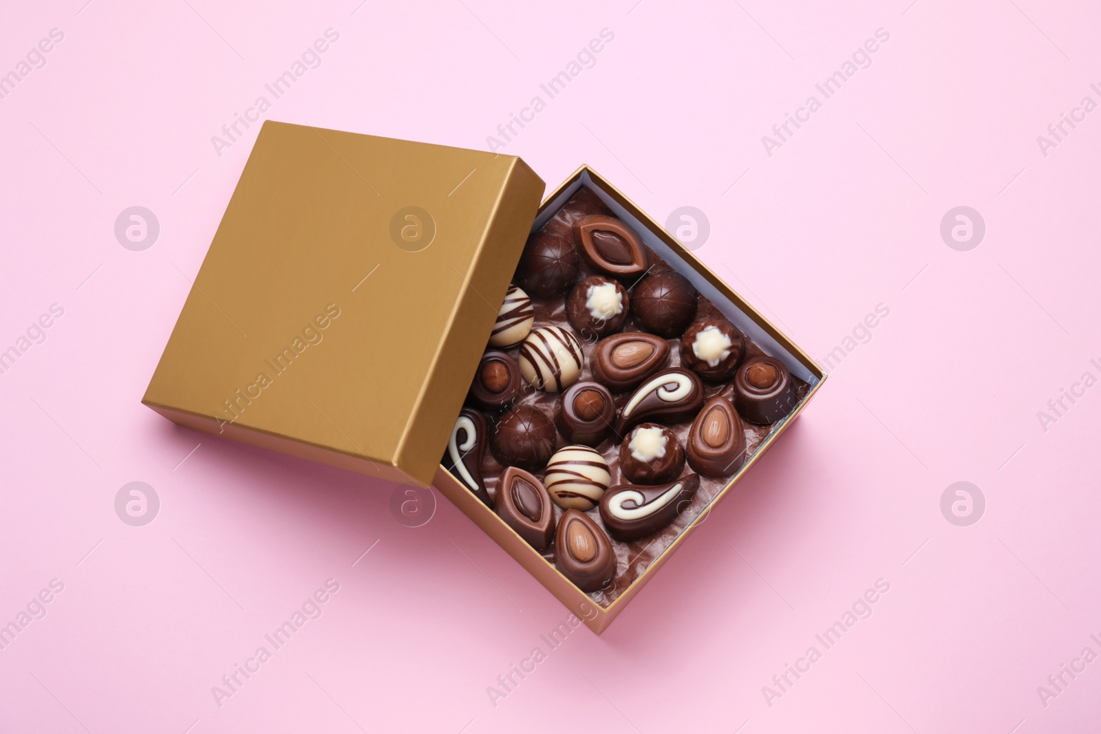 Photo of Open box of delicious chocolate candies on pink background, flat lay