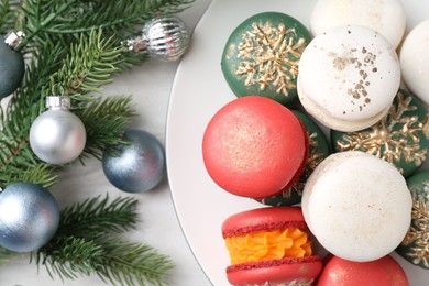 Photo of Different decorated Christmas macarons and festive decor on white wooden table, above view