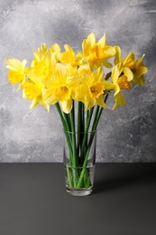 Photo of Bouquet of beautiful yellow daffodils in vase on grey wooden table