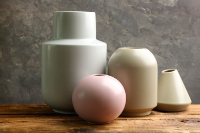 Stylish empty ceramic vases on wooden table against grey background