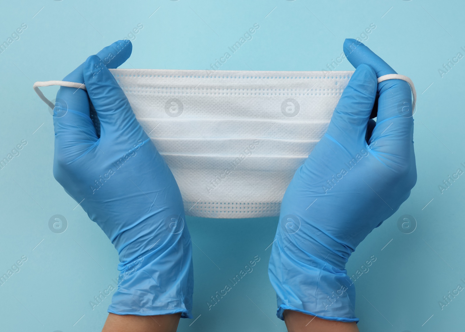 Photo of Doctor in medical gloves holding protective mask on light blue background, closeup