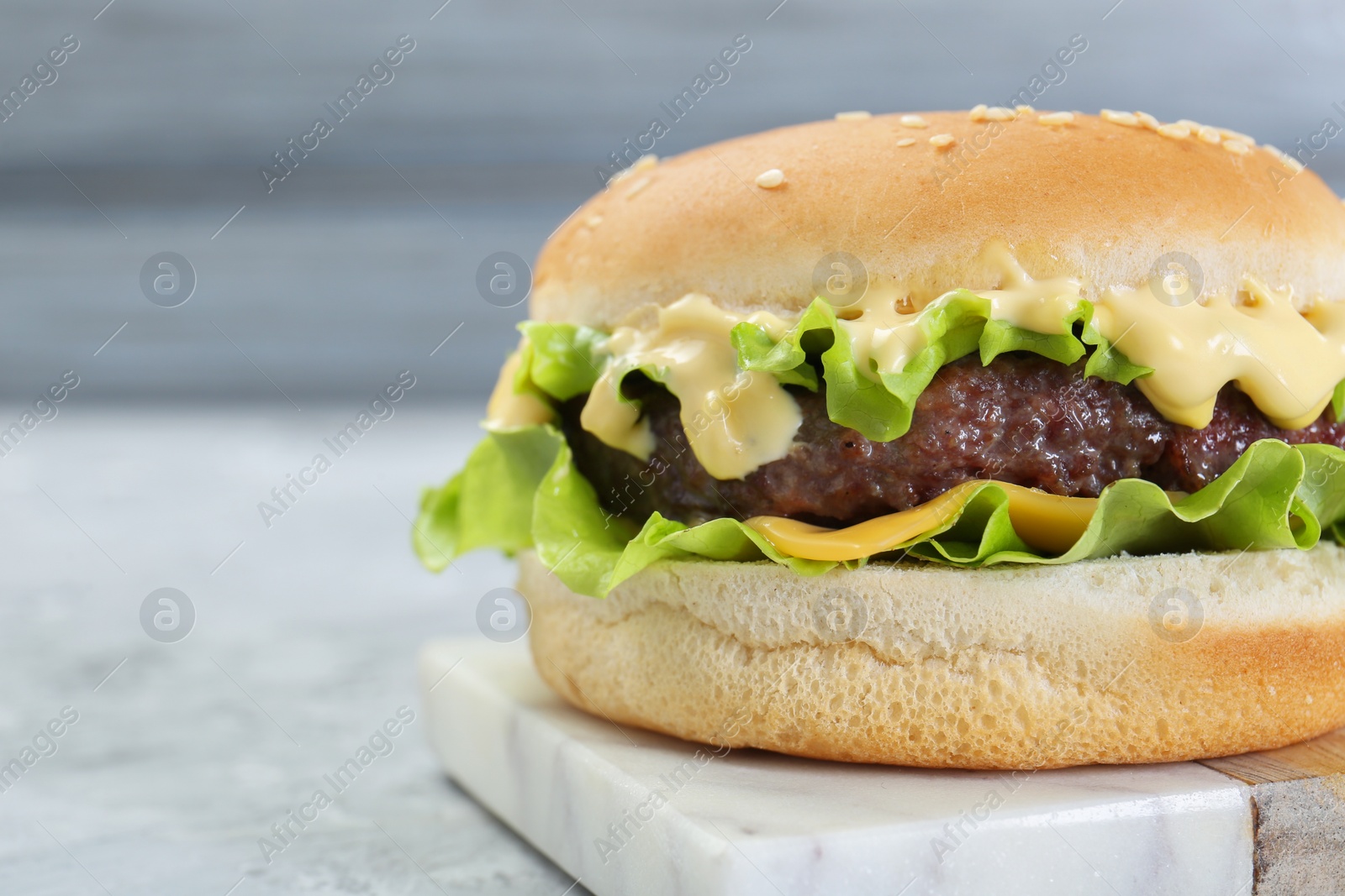 Photo of Delicious cheeseburger on grey textured table, closeup. Space for text