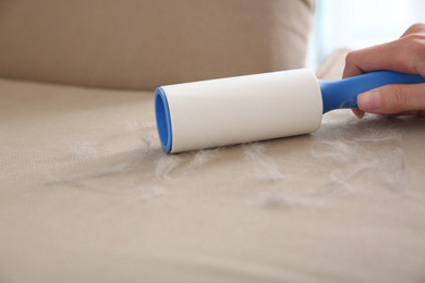 Woman removing hair from beige sofa, closeup