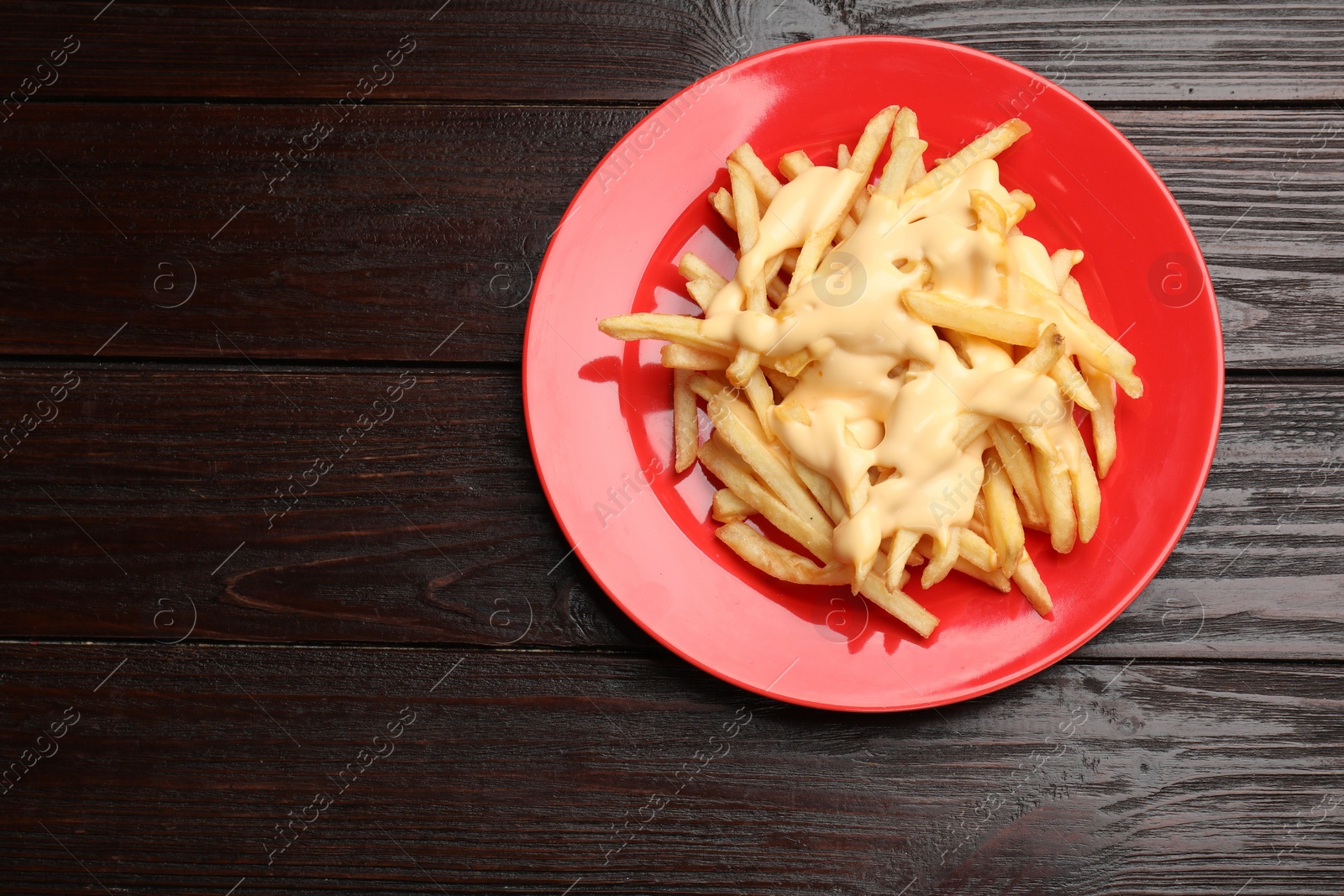 Photo of Delicious french fries with cheese sauce on wooden table, top view. Space for text