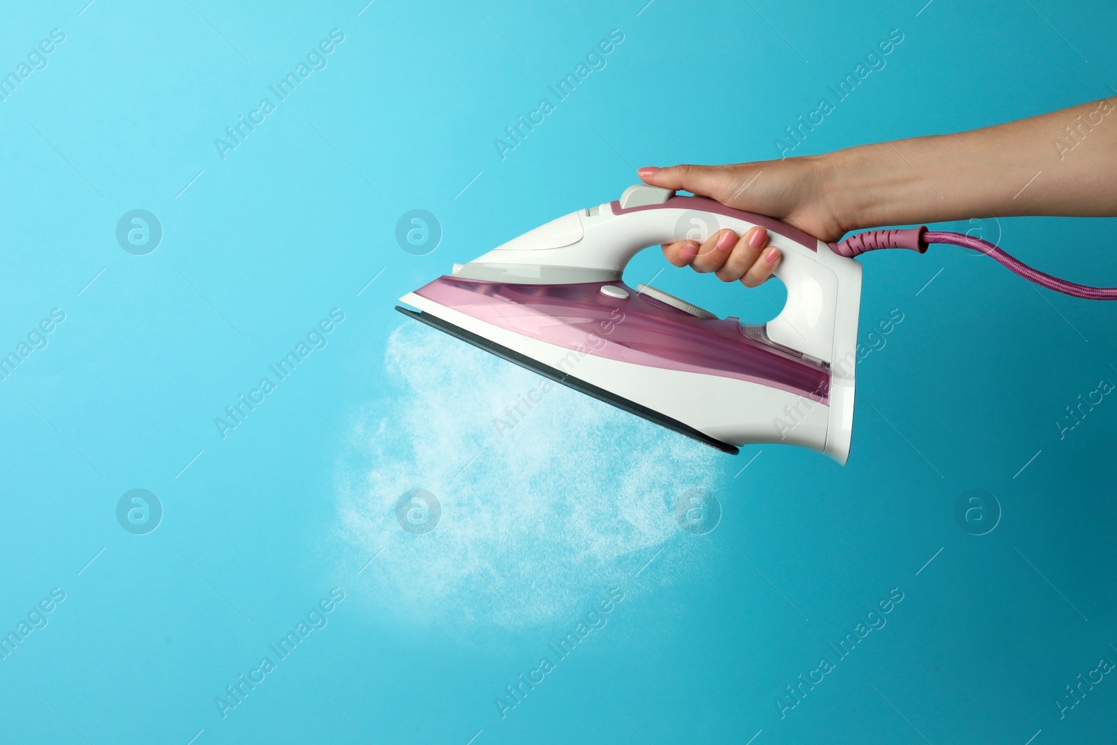 Image of Woman holding modern iron with steam on turquoise background, closeup. Space for text