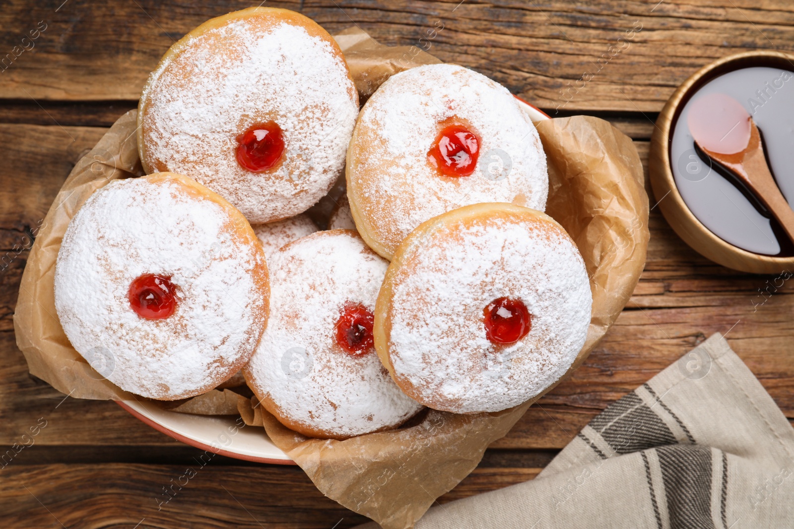 Photo of Delicious donuts with jelly and powdered sugar in baking dish on wooden table, flat lay