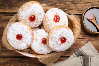 Delicious donuts with jelly and powdered sugar in baking dish on wooden table, flat lay