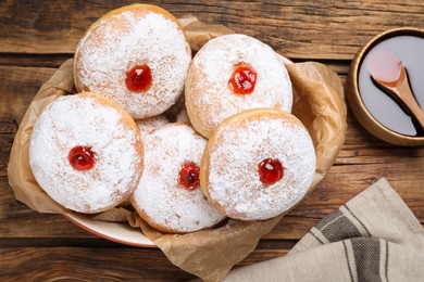 Photo of Delicious donuts with jelly and powdered sugar in baking dish on wooden table, flat lay