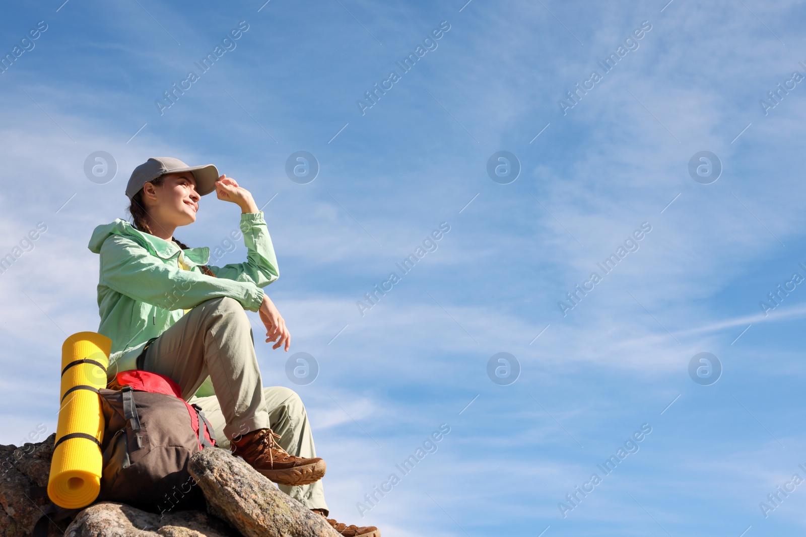 Photo of Young woman with backpack and sleeping mat on cliff. Space for text