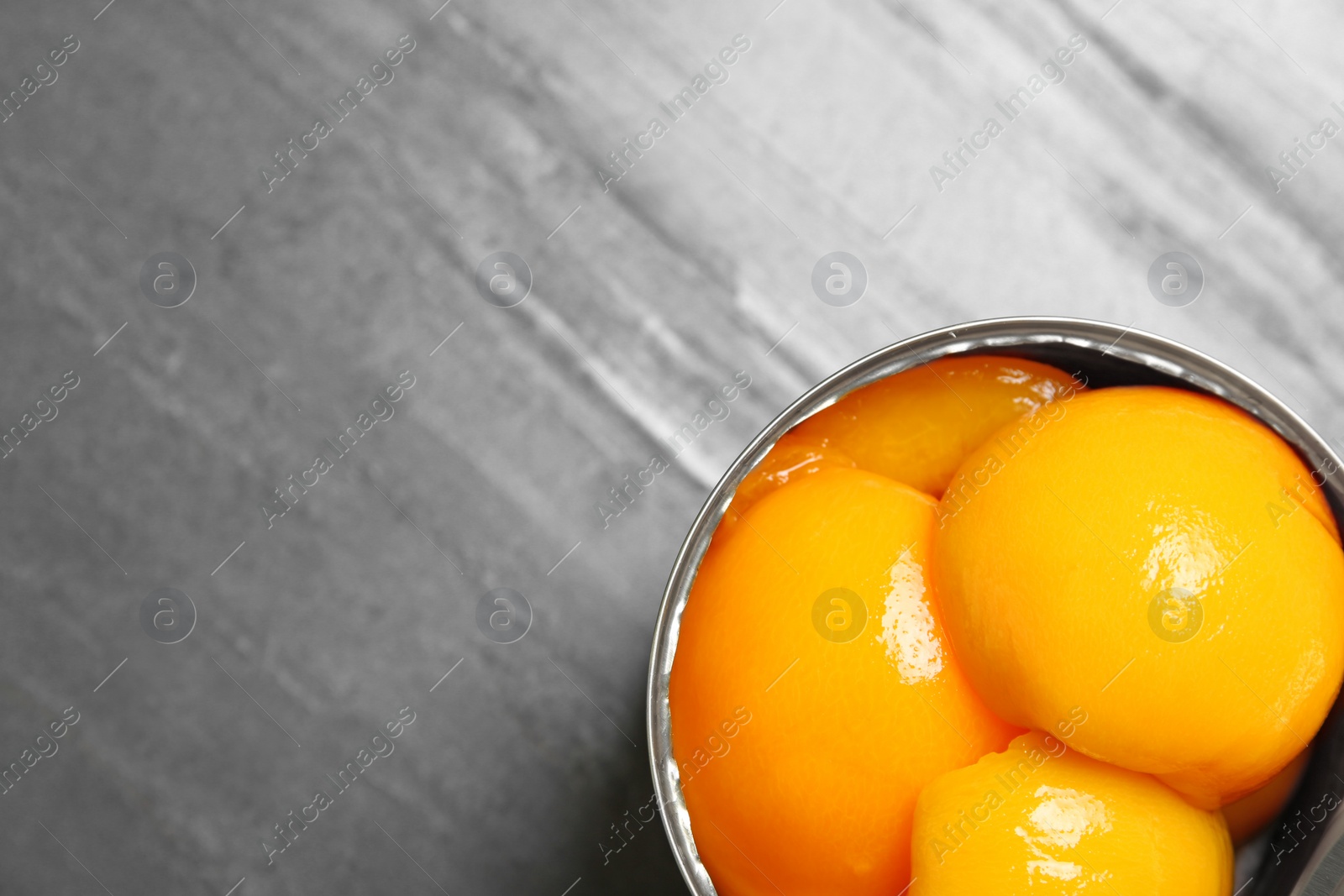 Photo of Open tin can of peaches on grey background, top view with space for text