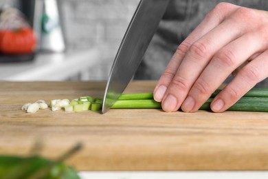 Photo of Woman cutting green spring onion on wooden board at table, closeup