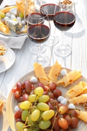 Photo of Red wine and snacks served for picnic on white wooden table