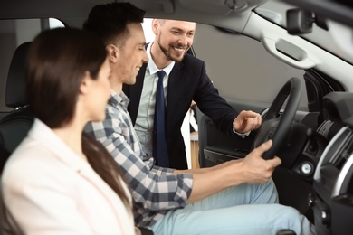 Salesman consulting young couple in auto at dealership. Buying new car