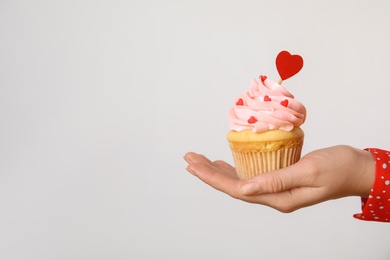 Closeup view of woman holding tasty cupcake on light background, space for text. Valentine's Day celebration