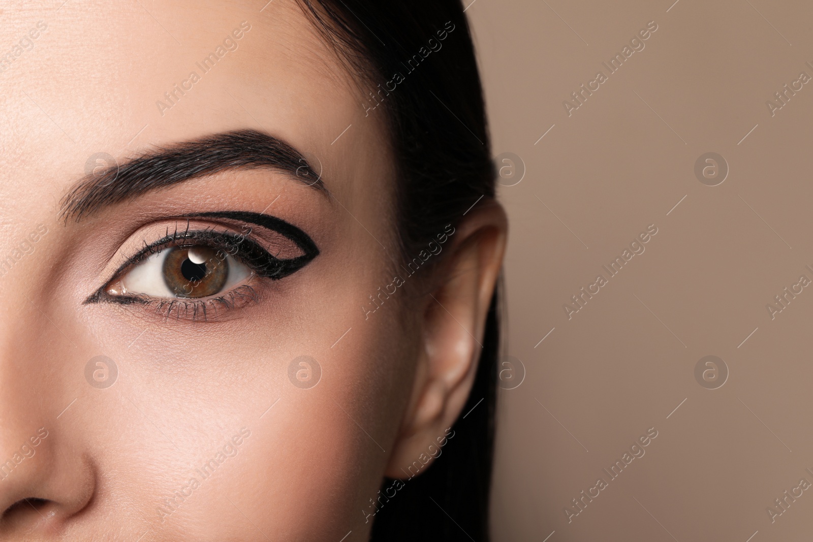 Photo of Beautiful woman with black eyeliner on beige background, closeup. Space for text