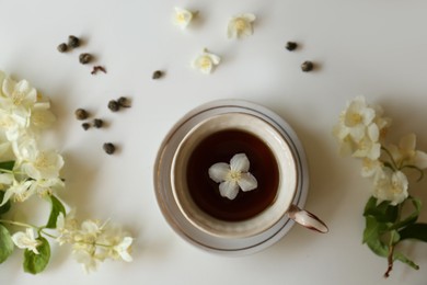 Photo of Beautiful jasmine flowers and cup of aromatic tea on white table, flat lay