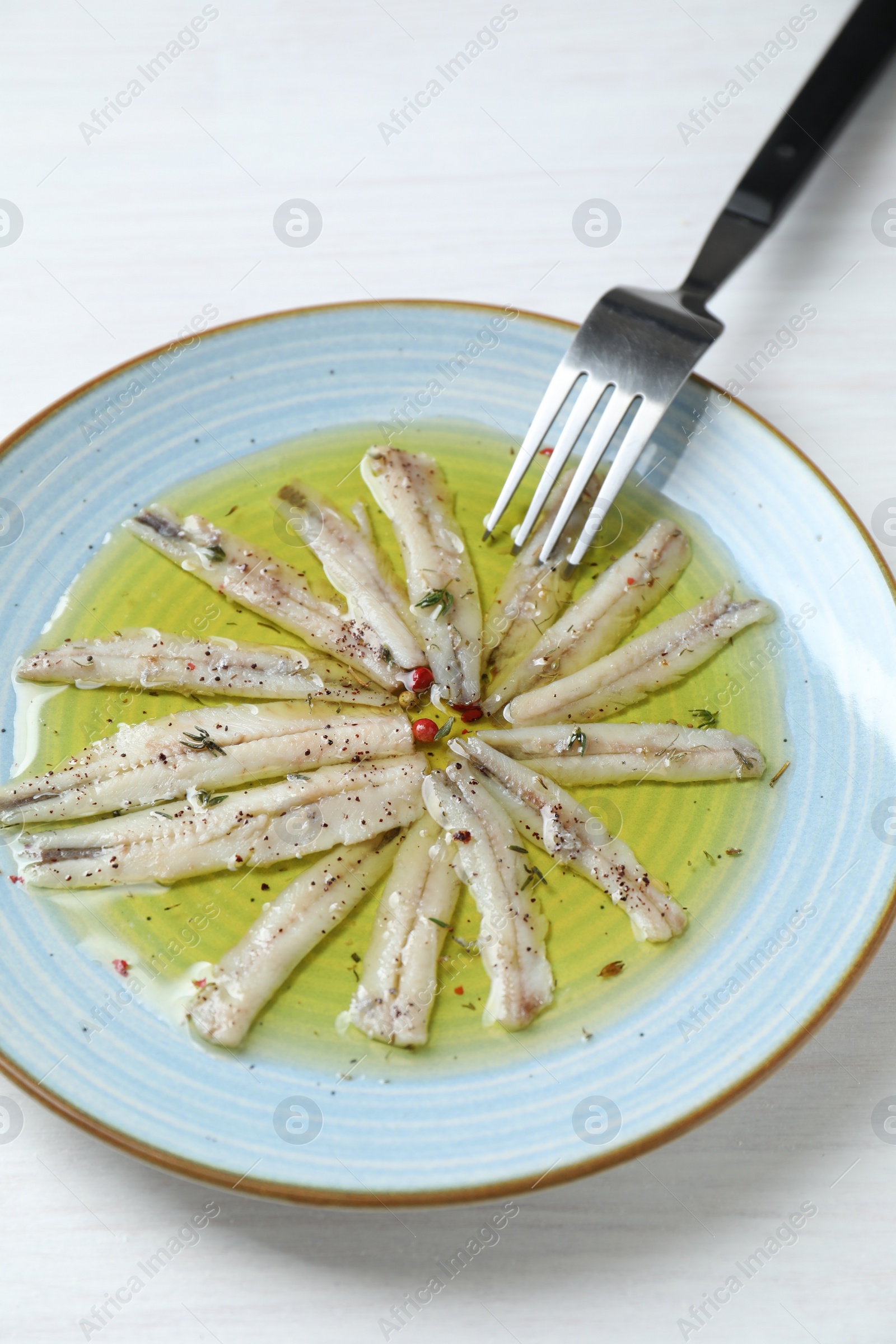 Photo of Tasty pickled anchovies with spices on white wooden table, above view