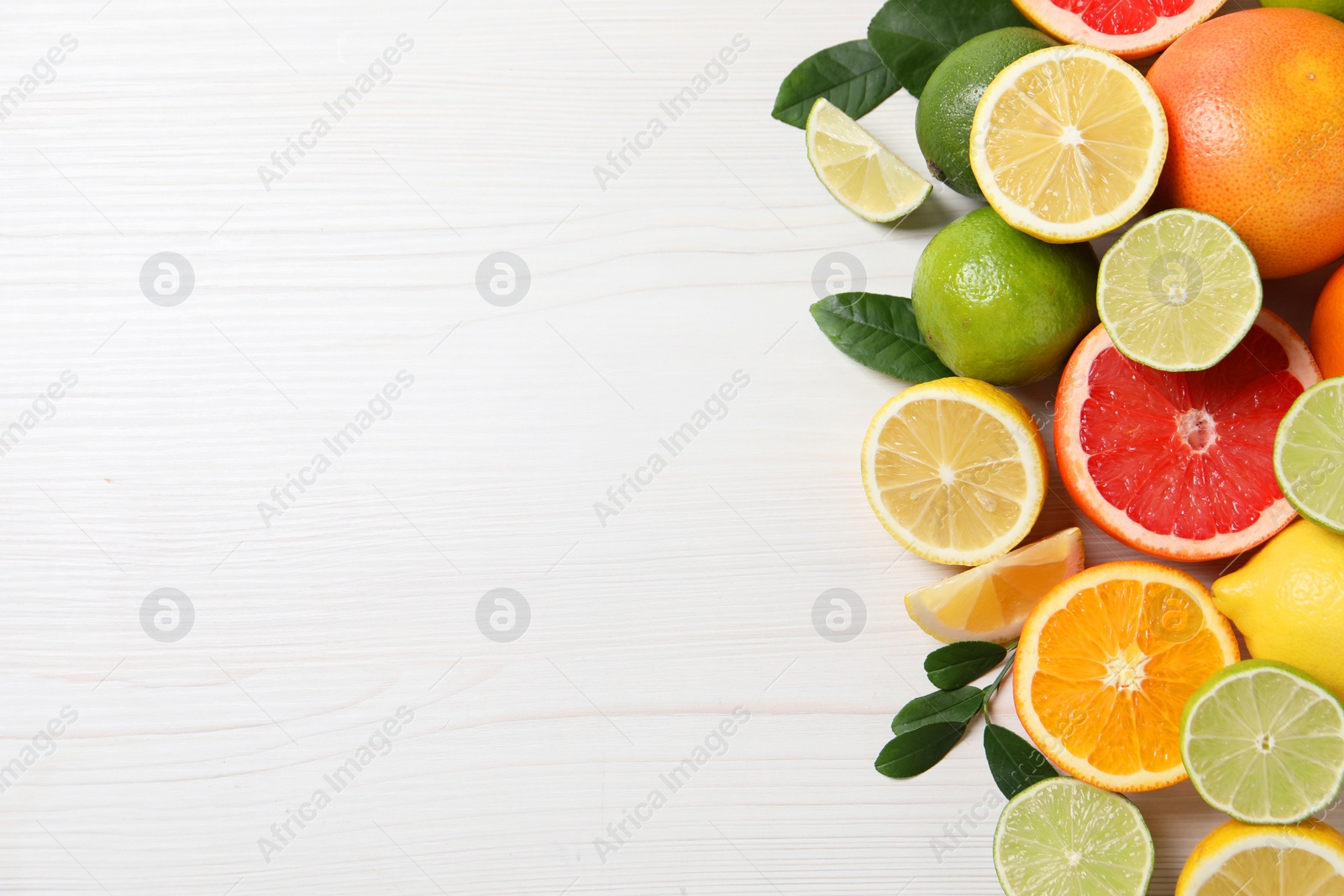 Photo of Different cut and whole citrus fruits on white wooden table, top view. Space for text