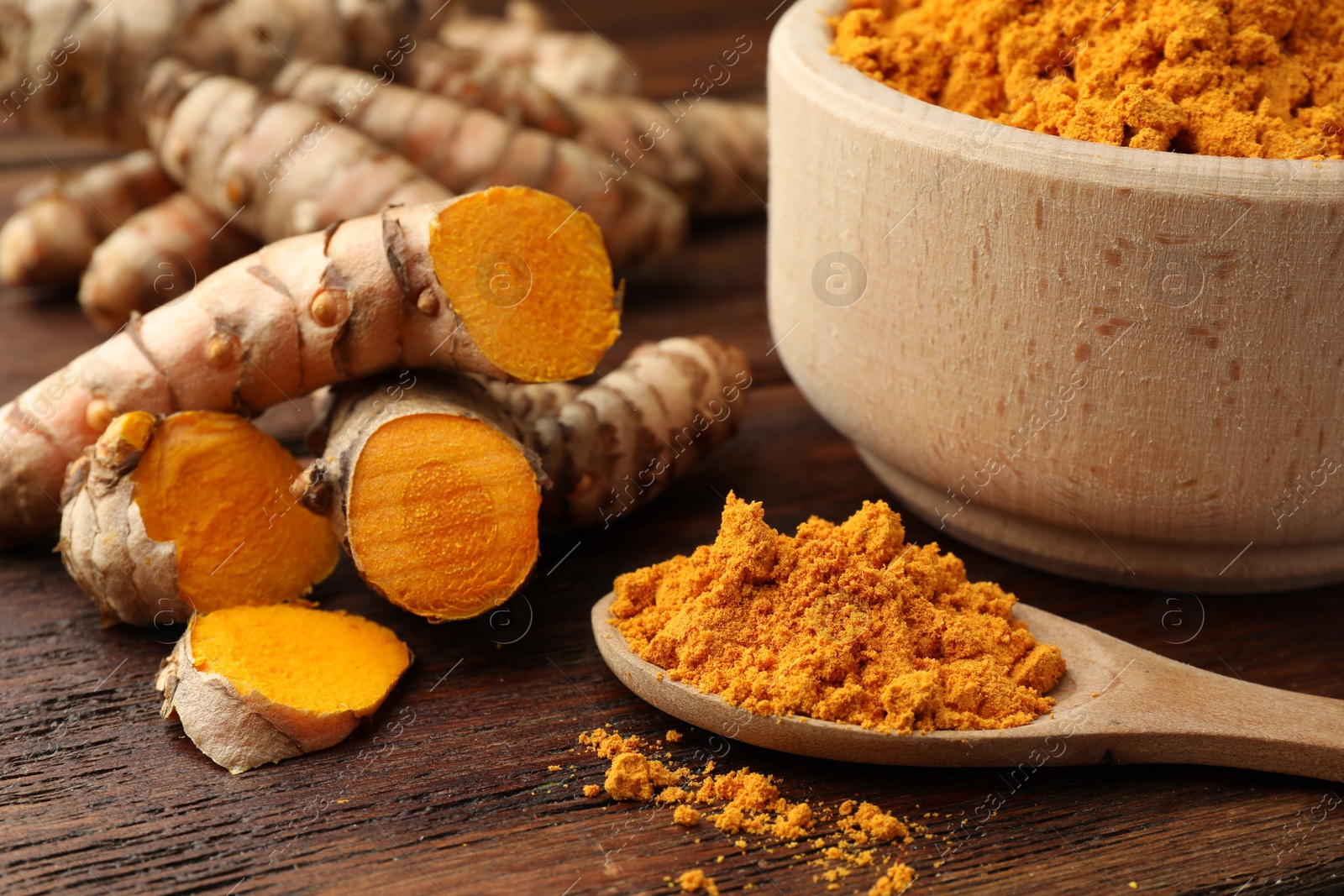 Photo of Aromatic turmeric powder and raw roots on wooden table, closeup