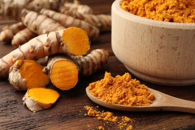 Aromatic turmeric powder and raw roots on wooden table, closeup