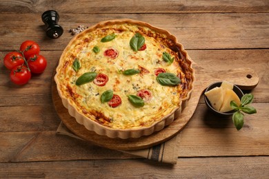 Photo of Delicious quiche with cheese, tomatoes and basil on wooden table