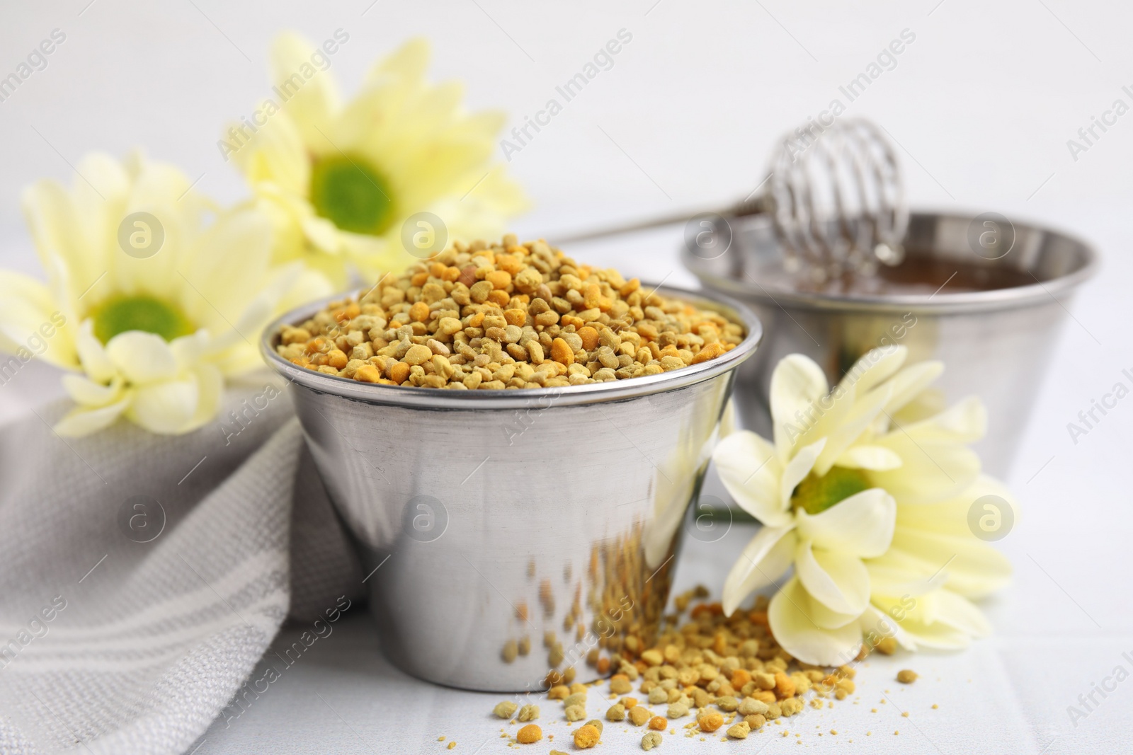 Photo of Fresh bee pollen granules and flowers on white table, closeup